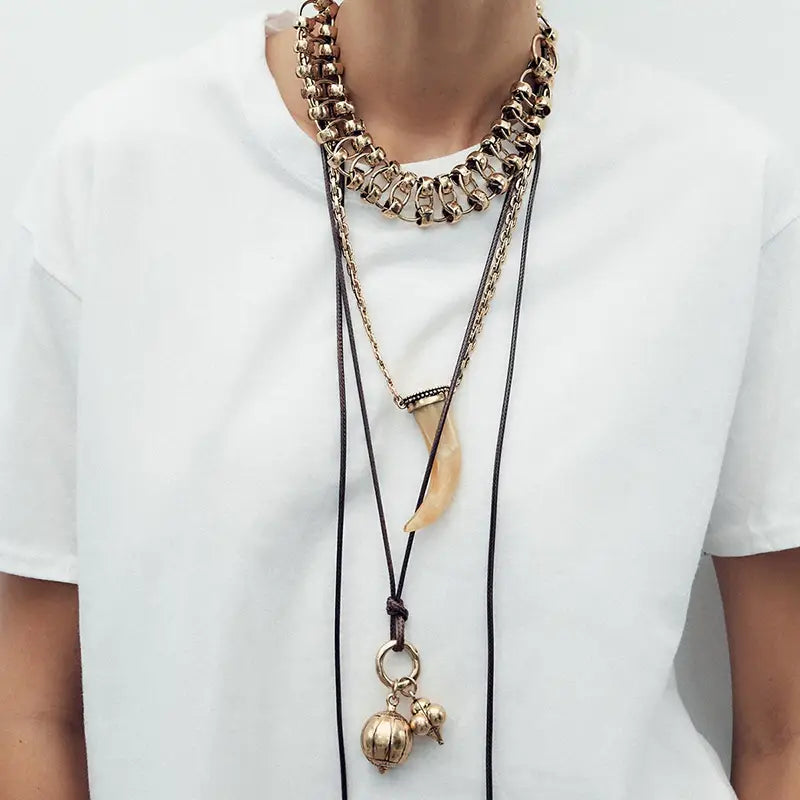 vintage ethnic layered pendant necklace for women featuring gold-toned chunky chains with black cord tassels and ivory-colored horn charm pendants.
