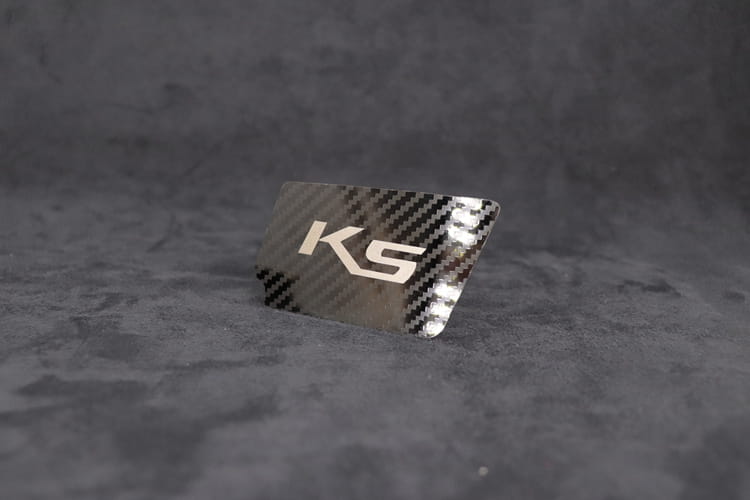 シルバーのksロゴを備えたカーボンファイバーのプレートを特徴とする、Kia K5 スエードカーボン インテリア ドアハンドルカバー。
