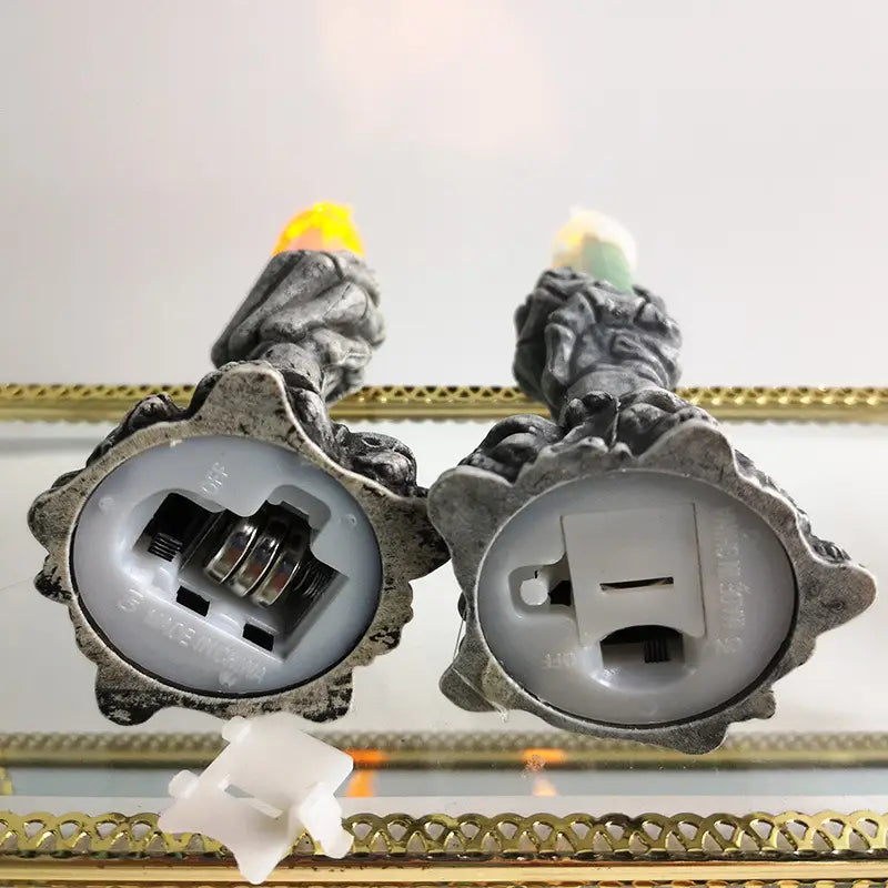 two gray textured led candles with glowing yellow and green flames shaped like skeleton hands for a party happy halloween celebration