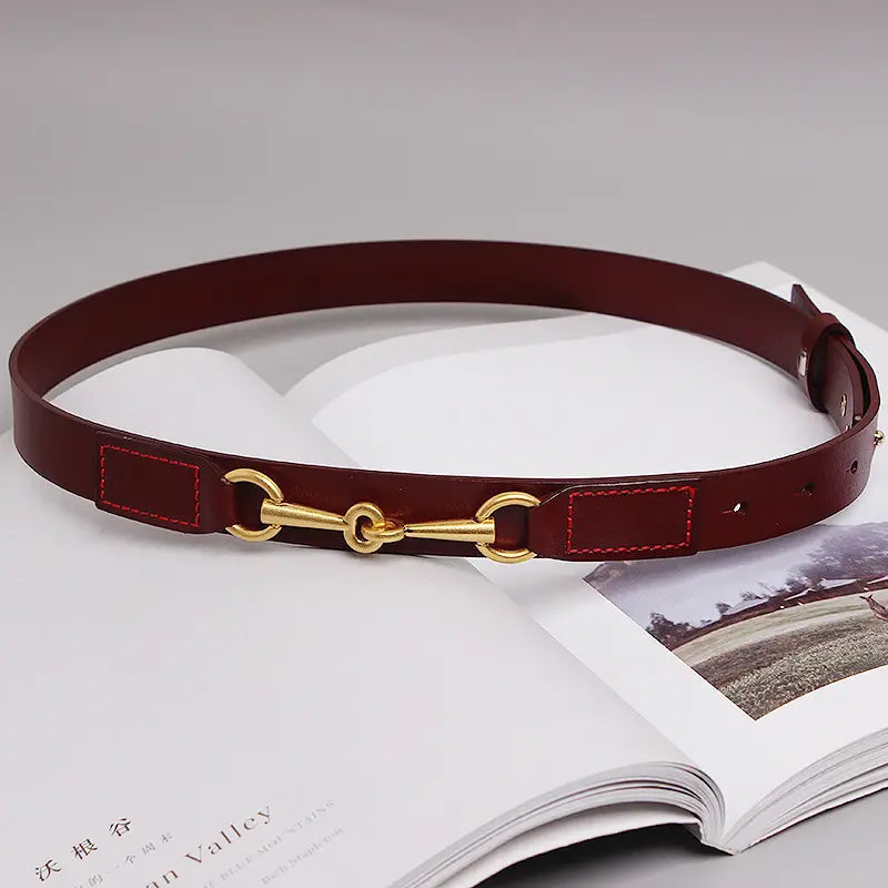 A women leather belt in burgundy leather featuring a polished gold-tone horsebit buckle and contrasting red stitching.
