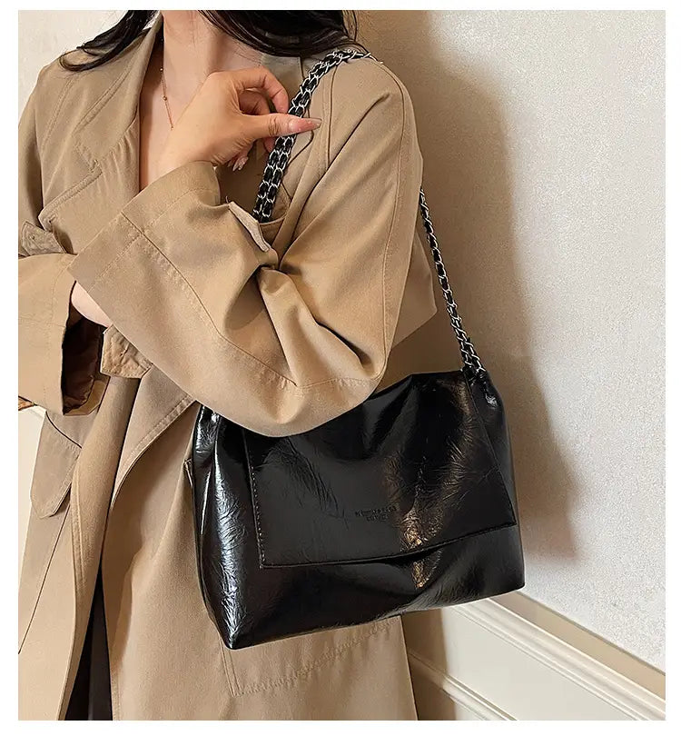 Bolso bandolera negro de charol brillante con correa de cadena, que muestra un diseño de gran capacidad, para un uso versátil entre los bolsos bandolera.