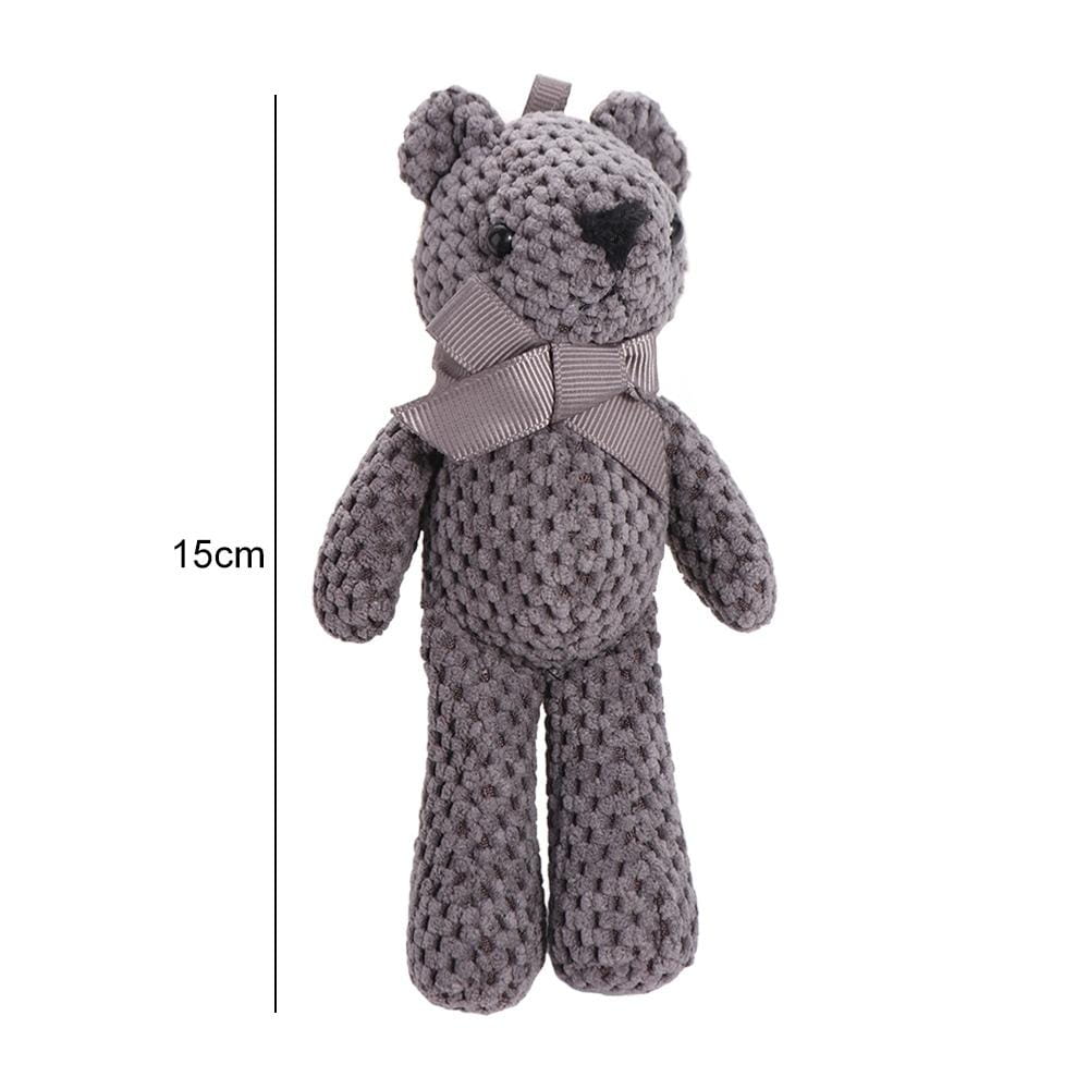 Une peluche d’ourson teddy au crochet faite à la main, en gris doux, à texture côtelée, avec des yeux et un nez à boutons noirs, ainsi qu’un ruban assorti noué autour du cou.