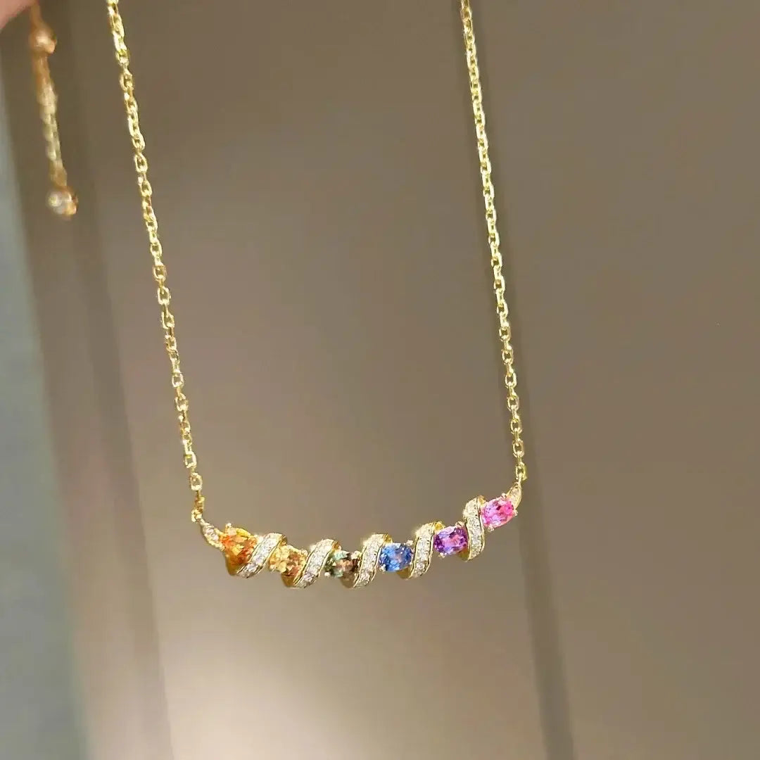 Un collier en argent, avec une chaînette délicate en or, surmontée d'un pendentif barre courbée orné de cinq pierres précieuses facettées colorées en orange, vert, bleu, violet et rose, montées dans un ouvrage métallique torsadé minutieux.