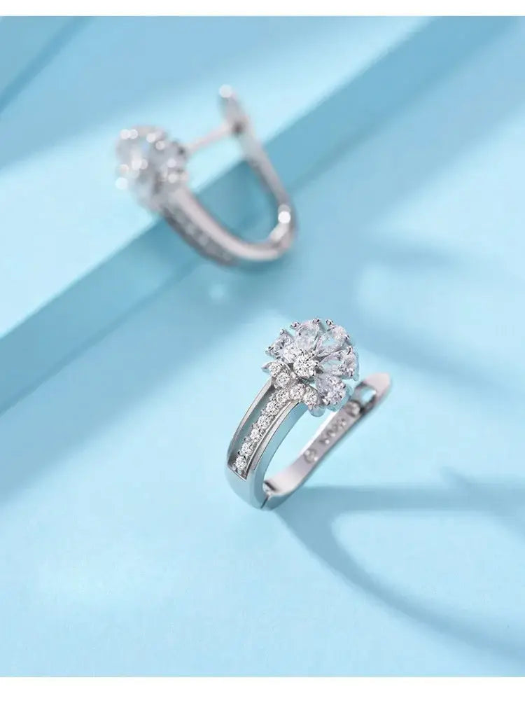 Los pendientes de flores de circonio en plata de ley presentan un diseño de aro plateado con un conjunto central de diamantes brillantes rodeado por piedras más pequeñas a lo largo de la banda.