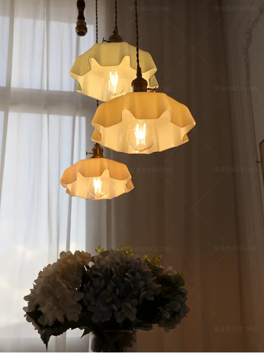 Trois luminaires suspendus à jupe florale en verre de couleur crème, avec une tête de lampe en cuivre suspendue au plafond visible depuis le dessous.