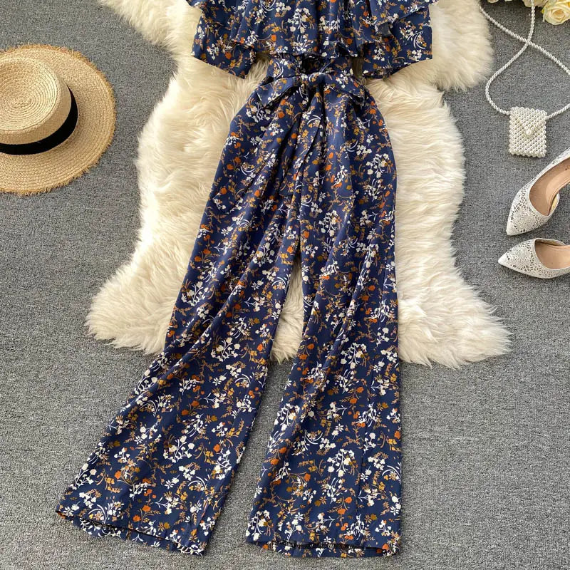 Enterizo de pierna ancha con estampado floral azul marino con escote tipo bardot, mangas con volante y cinturilla atada para un uso casual elegante.