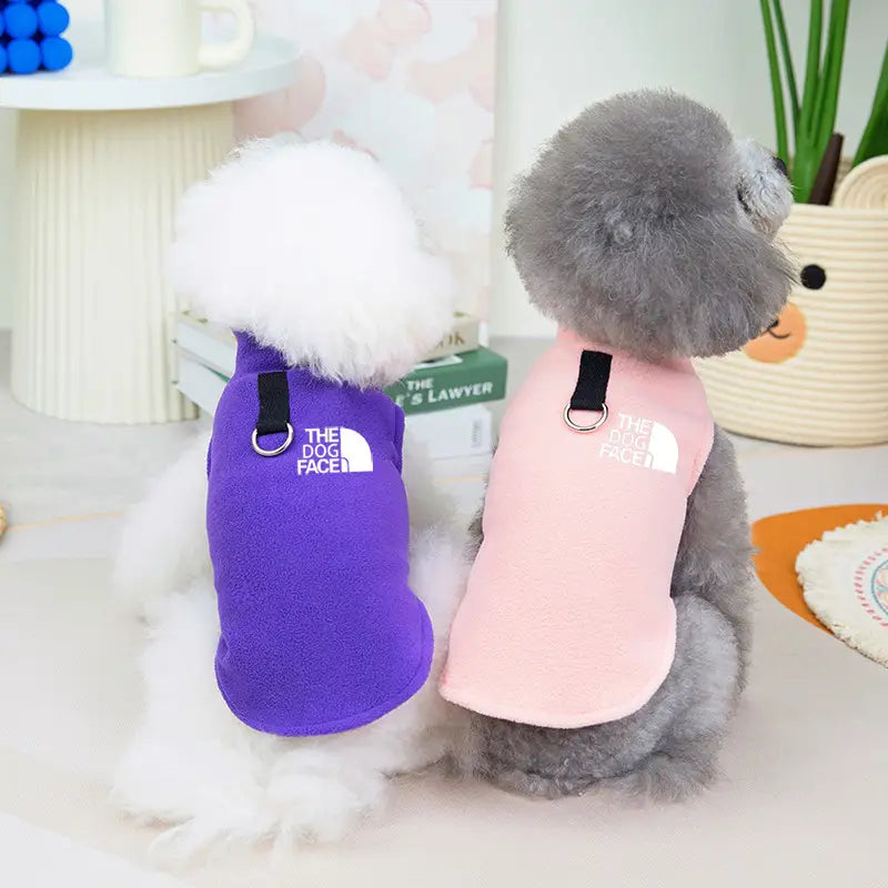Lila- und pinkfarbene flauschige warme Hundewesten für kleine bis mittelgroße Hunde mit schwarzen Trägern, silbernen Metallringen und dem Hundegesichts-Logo in Weiß, sichtbar auf der Rückseite