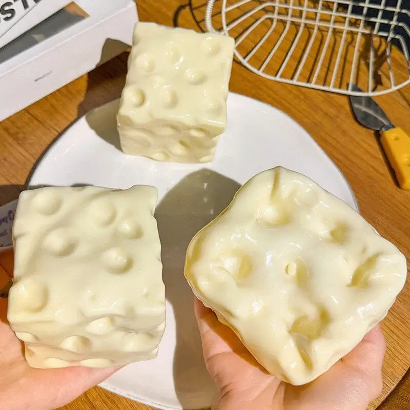 cream-colored cube-shaped cheese squishy toy with glossy finish and realistic holes for stress relief shown from a front angle