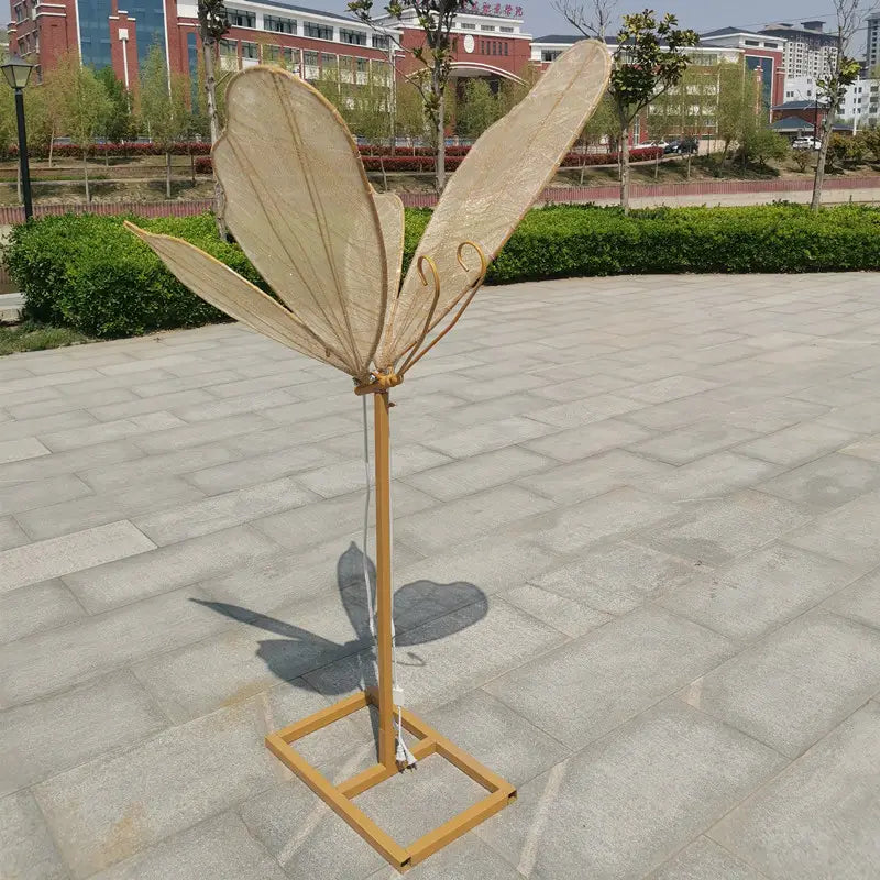 Ein beige blattförmiger dekorativer Fächer mit Bambusstab und hölzerner Basis, verwendet als leuchtende, an der Decke hängende Hochzeitstennenlichtanlage mit Schmetterlingsflügeln.