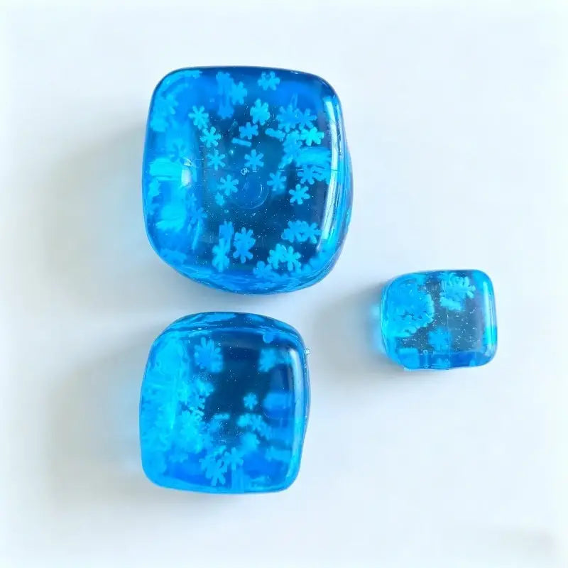 Drei durchscheinende blaue Eiswürfel mit Schneeflocken-Motiv zur Stressreduktion aus Harz, jeweils mit eingebetteten Schneeflockenmuster aus einem frontalen Blickwinkel sichtbar.
