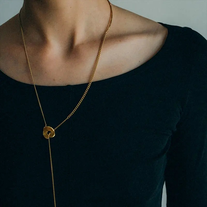 Collier en chaîne aux tons dorés pour femmes, présentant un pendentif circulaire avec un trou centré dans un design à superposition géométrique.