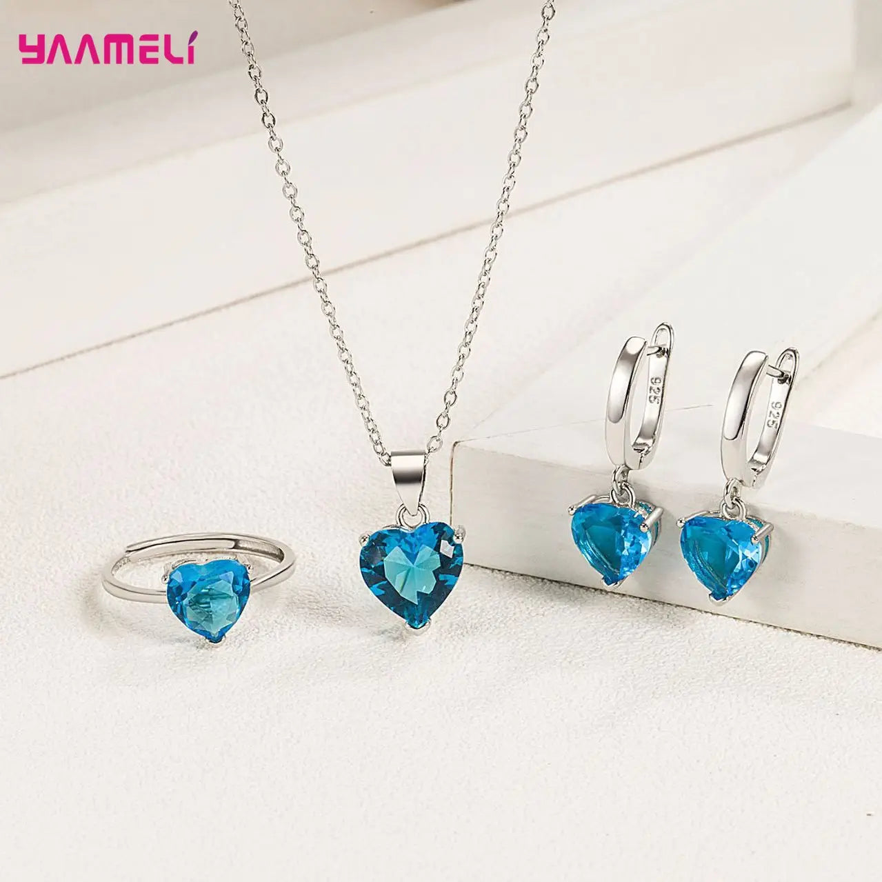 A sterling silver heart jewelry set featuring vibrant blue zircon gemstones with an adjustable necklace chain, matching hoop earrings, and a ring.