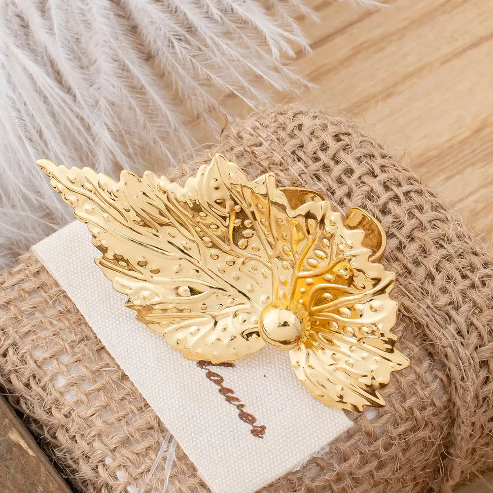 Parure de bijoux en perles et feuilles d’or, comprenant une broche dorée en forme de feuille, avec des détails complexes et un accent central évoquant une perle.