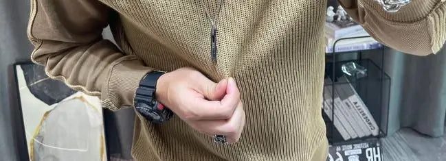 Montre numérique noire avec bracelet texturé et bouton d’accent rouge, présentée aux côtés d’un pull-over en maille à empiècement contrastant pour homme, manches longues.