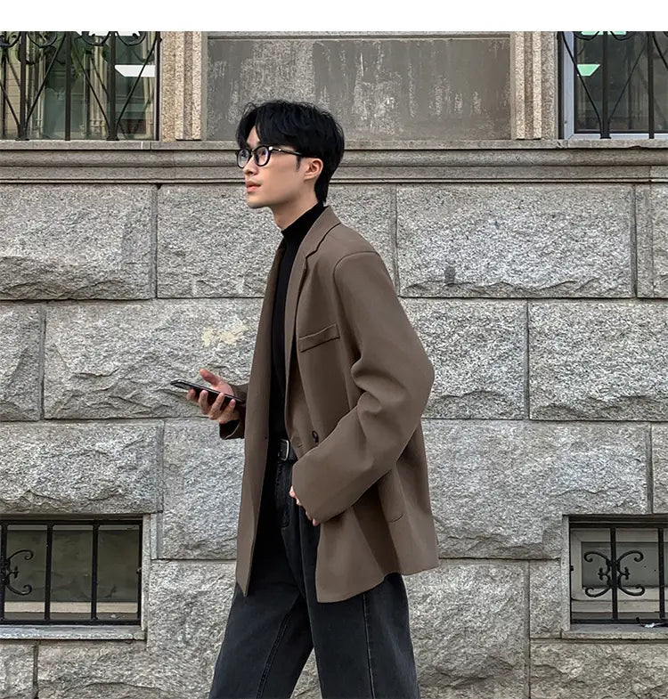Una blazer de doble botonadura en poliéster color marrón, elegante, con ajuste relajado y hombros estructurados, usada sobre un cuello vuelto negro para uso casual de hombre.