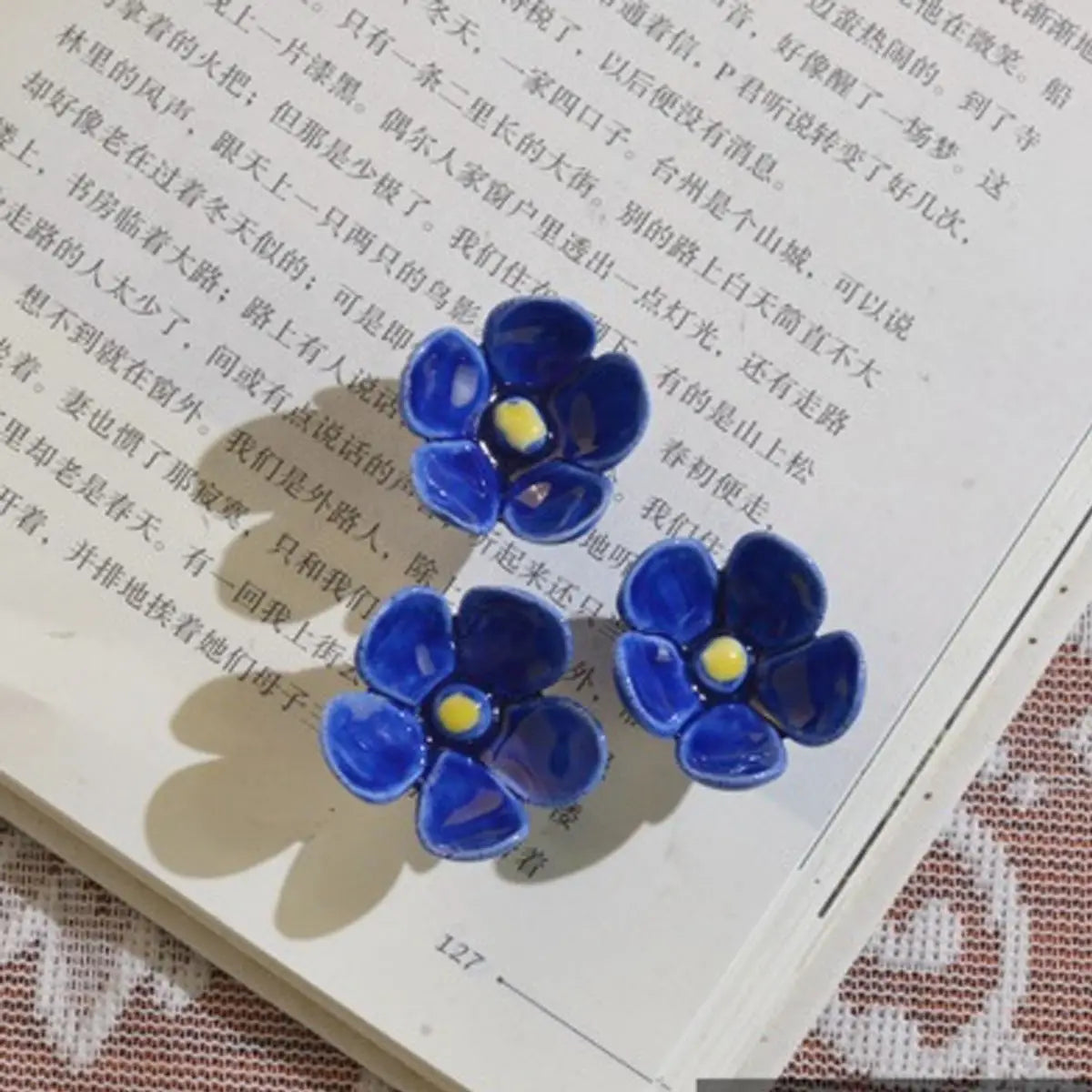 Deep blue ceramic artificial flowers shaped as forget me nots with yellow centers ideal for decorating vases.