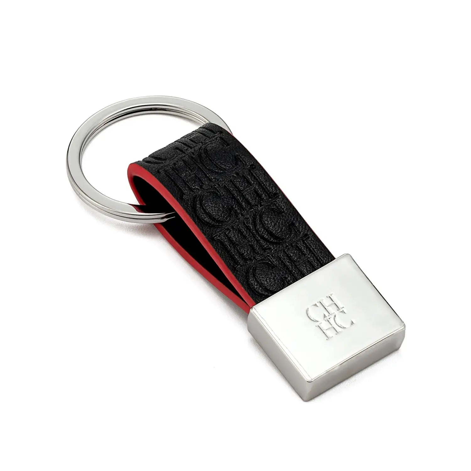 Porta llaves de cuero negro con forro interior rojo y logotipo en relieve en el que se incorpora una placa metálica de tono plateado grabada con ch hc, como accesorio de equipaje minimalista.