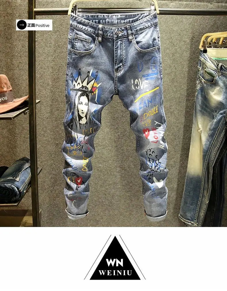 Jean slim stretch imprimé pour homme en denim bleu, présentant un design vibrant de style graffiti avec une femme couronnée formant des cœurs et un texte incluant « love » et « dolce » affichés sur un cintre.