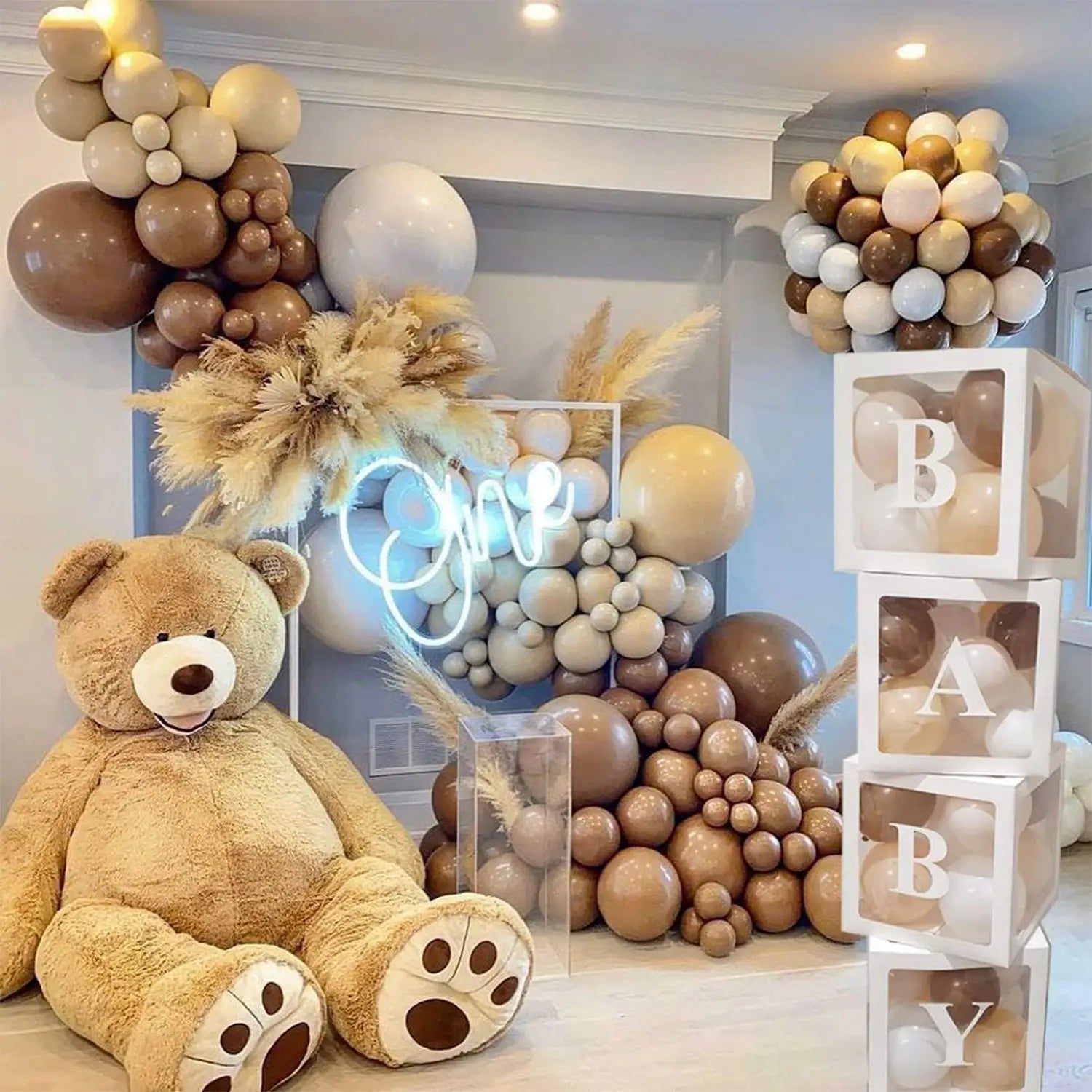 Ein kuscheliger beigefarbener Teddybär mit weißen Pfotenpolstern und angenähter Nase steht vor transparenten Buchstabenblöcken aus dem Baby-Dusch-Ballonboxen-Set, 4-teilig.