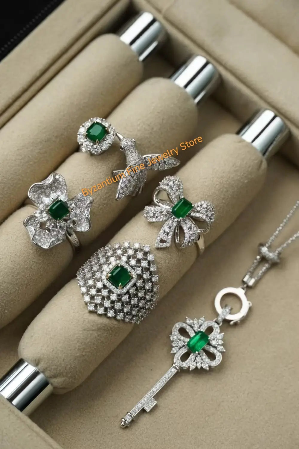 Ohrringe mit silbernen Tropfenquasten in Gold-Vermeil, kombiniert mit eleganten silbernen Schmuckstücken mit Smaragd- und Diamantakzenten, einschließlich blütenförmiger und schalenförmiger Ringe sowie einer Anhängerkette mit Schlüsselmotiv.