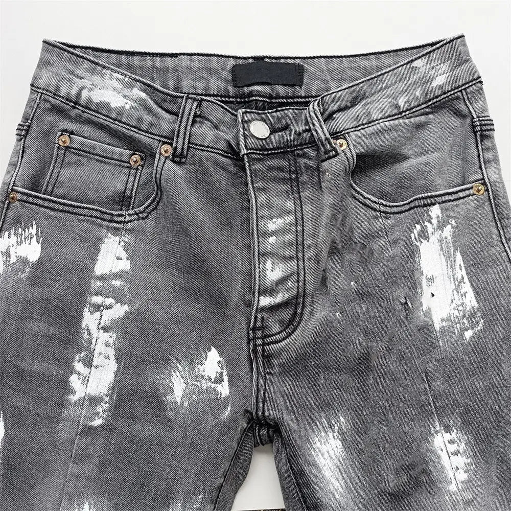 Jeans skinny déchirés pour hommes, effet délavé rétro vintage bleu, présentant un denim noir déchiré avec des accents d’éclaboussures de peinture blanches et des accessoires ton or.