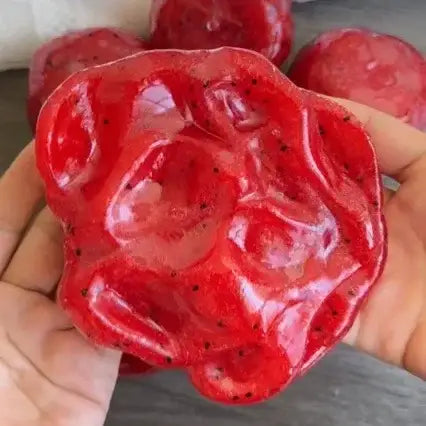 watermelon slushy squishy stress relief toy in the shape of a vibrant red dragon fruit with a glossy textured surface dotted with black seeds.