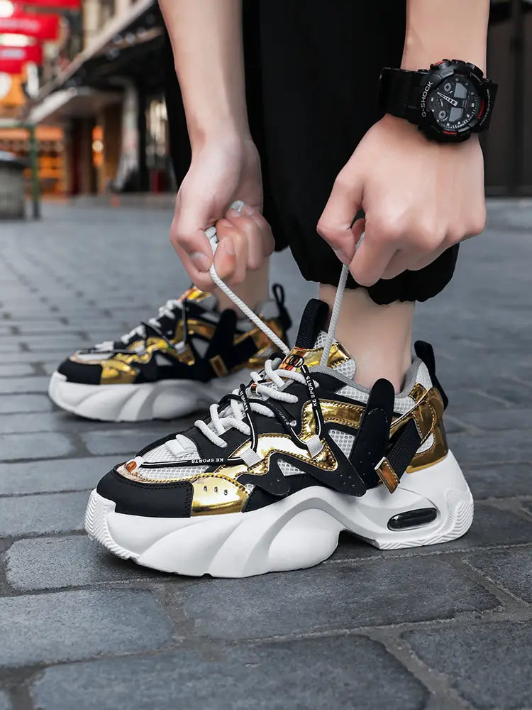 Men chunky air cushion casual sneakers in black and gold with white mesh accents and a thick cushioned sole.