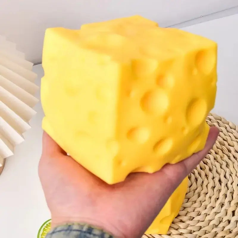 Un juguete antiestrés esponjoso con forma de cubo de queso, de color amarillo brillante, con orificios característicos y una textura suave y elástica.