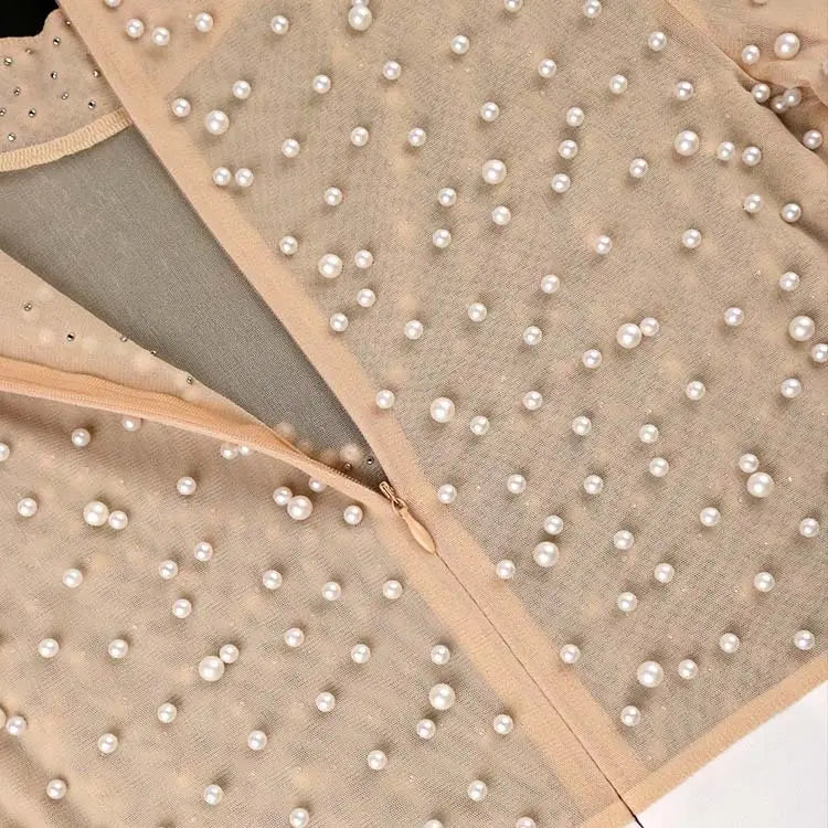 Beige beaded mesh jumpsuit with high waist featuring a sheer top adorned with scattered white pearls and a matching zipper for a party outfit.