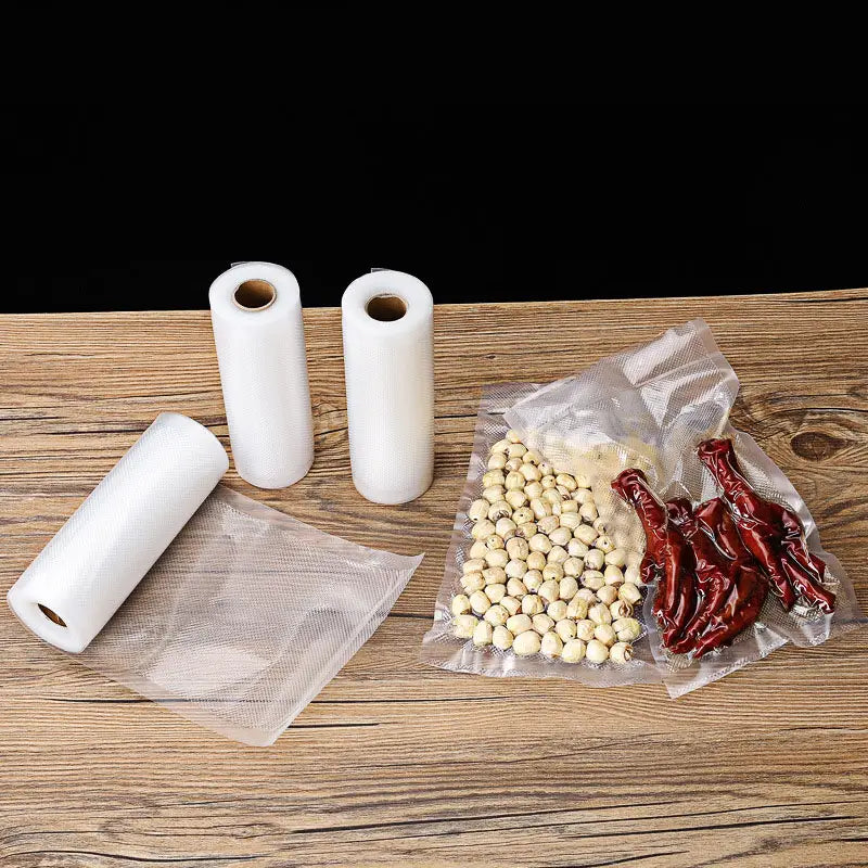 clear vacuum-sealed bags filled with white beans and red dried chilies next to three rolls of transparent plastic film for food vacuum sealer rolls 500cm storage bags.