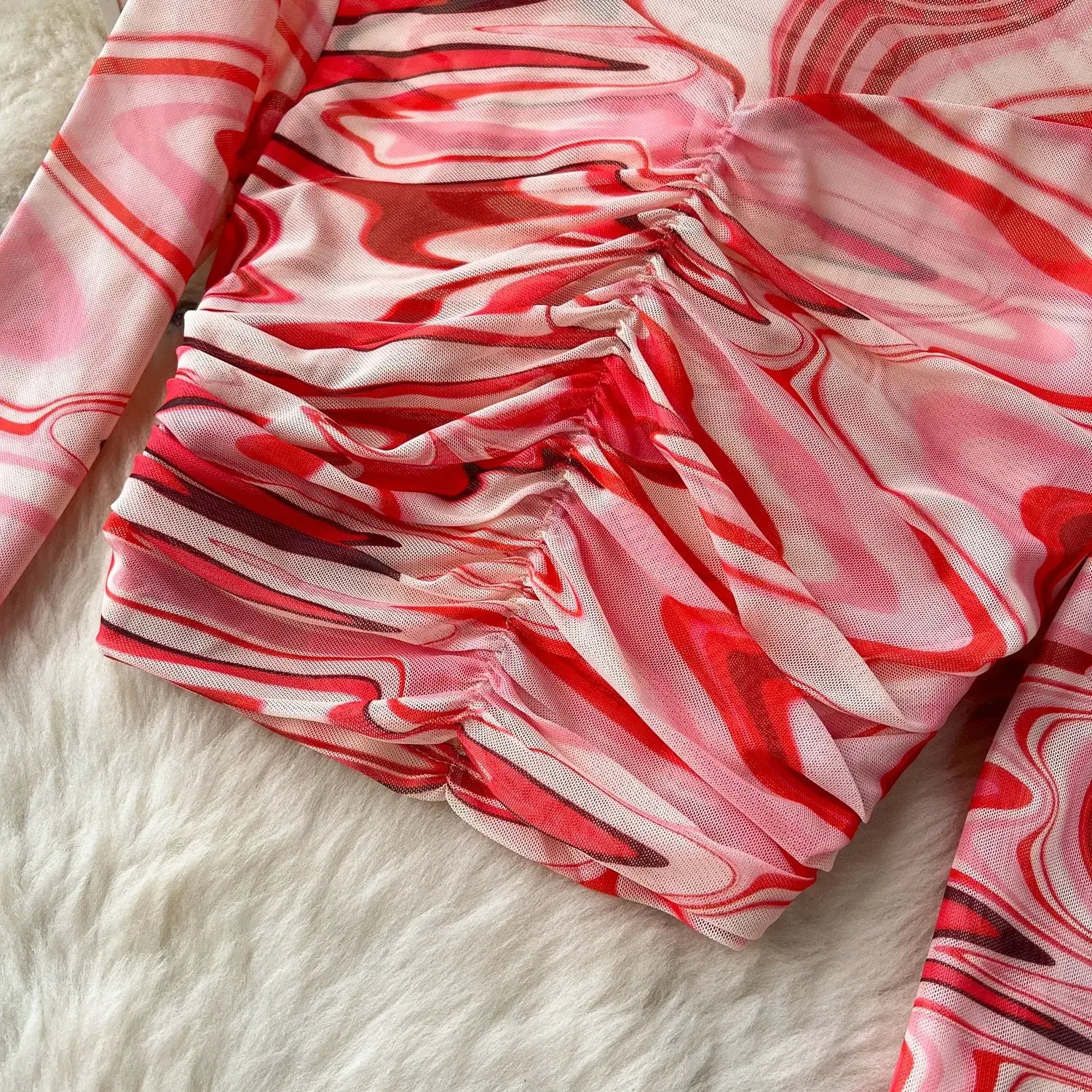 A ruched long-sleeved top in a flowing red and white marbled pattern made of lightweight fabric featuring an elastic closure as part of a two piece mesh skirt set marble print.