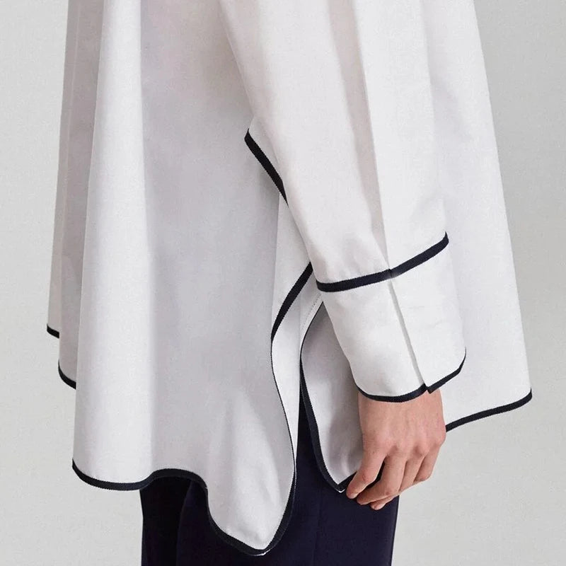 Bestickte Baumwollbluse mit fließendem asymmetrischem Design in Weiß mit schwarzer Zierborte entlang der Manschetten und des Saums.