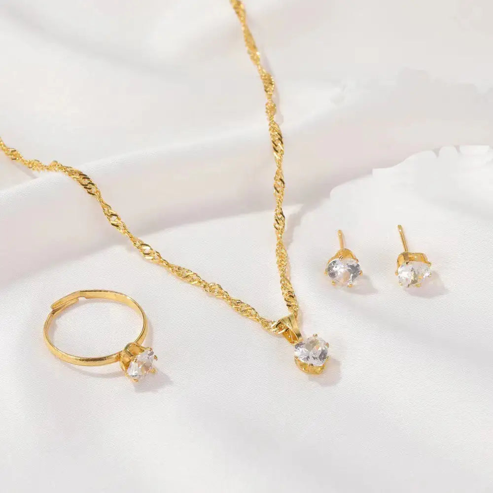 Juego de joyería de 5 piezas con circonitas cúbicas de color dorado, que incluye un collar de cadena trenzada con un dije central de piedra transparente, aretes tipo botón a juego y un anillo ajustable tipo banda, acentuado con piedras de circonita cúbica brillantes.