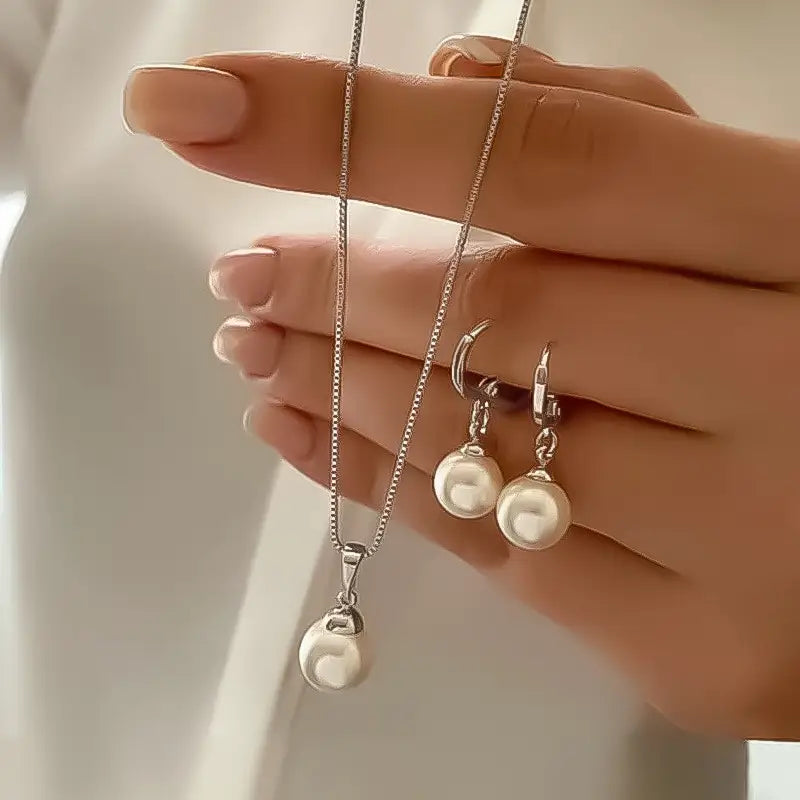 A delicate gold necklace with a single pearl pendant paired with matching gold hoop earrings featuring round pearls from the pearl jewelry set.