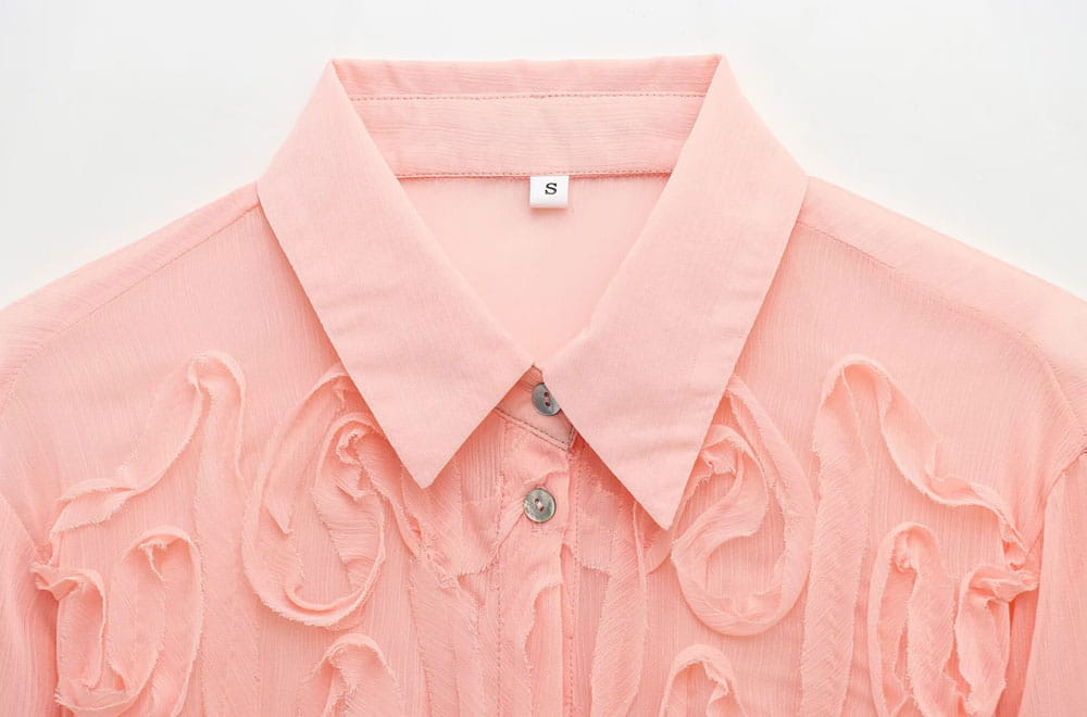 A delicate pink textured ruffled button up blouse with a classic collar and intricate ruffled detailing across the front.