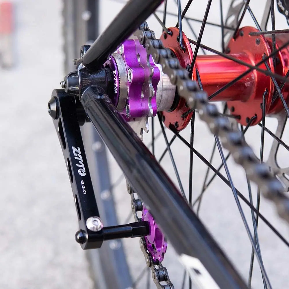 Purple aluminum alloy bike chain tensioner stabilizer with a silver center mounted on a red hub and black frame.