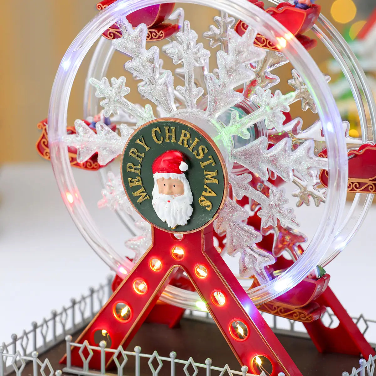 Ornement de manège forain musical de Noël festif en plastique rouge et transparent, avec des lumières illuminées et un emblème du Père Noël central sur une plaque circulaire verte.