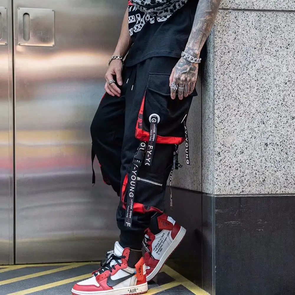 Pantalon cargo joggers streetwear pour hommes en noir, avec des accents rouges et des bretelles à marque, conçu pour une tenue décontractée.