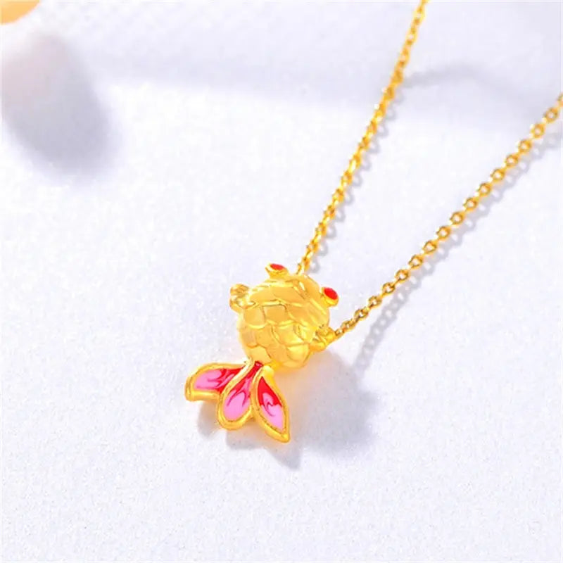 Collier pendentif poisson en or 24 carats délicat, présentant un corps doré brillant, des nageoires émaillées roses et des yeux sertis de pierres rouges.
