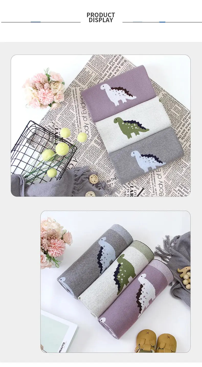 Set aus drei weichen, pastellfarbenen Stricksocken in Weiß, Grün und Grau mit verspielten Dinosaurier-Designs, die die Dinosaurier-gestrickte Babyddecke aus Baumwolle für die Wickeldecke im Gitterbett ergänzen.