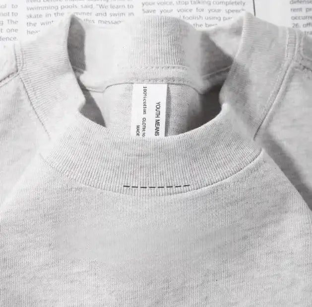 Sudadera de cuello tipo tripulante en color gris, confeccionada en 100 % algodón, con una etiqueta blanca que indica “youth” (juventud), mostrada junto a una camiseta de algodón de cuello redondo color azul marino.