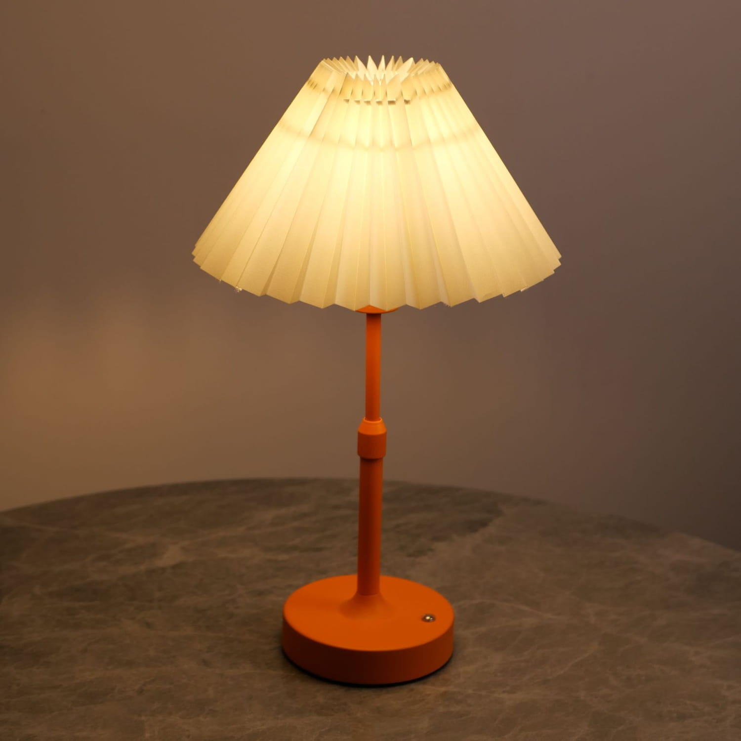 Eine warm orangefarbene Touch-Tischlampe mit einem plissierten cremefarbenen Papierschirm, aus dem vorderen Winkel dargestellt.
