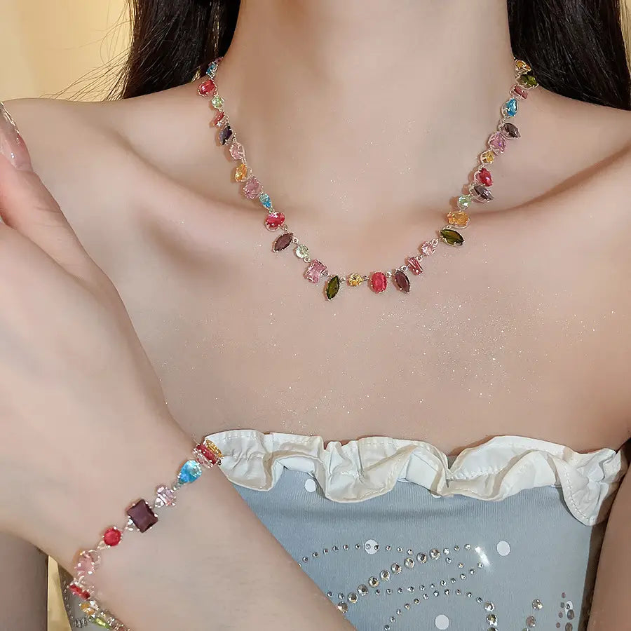 A delicate multicolored zircon crystal gold plated necklace and matching bracelet with vibrant red blue green pink and purple gemstones on a gold toned chain.