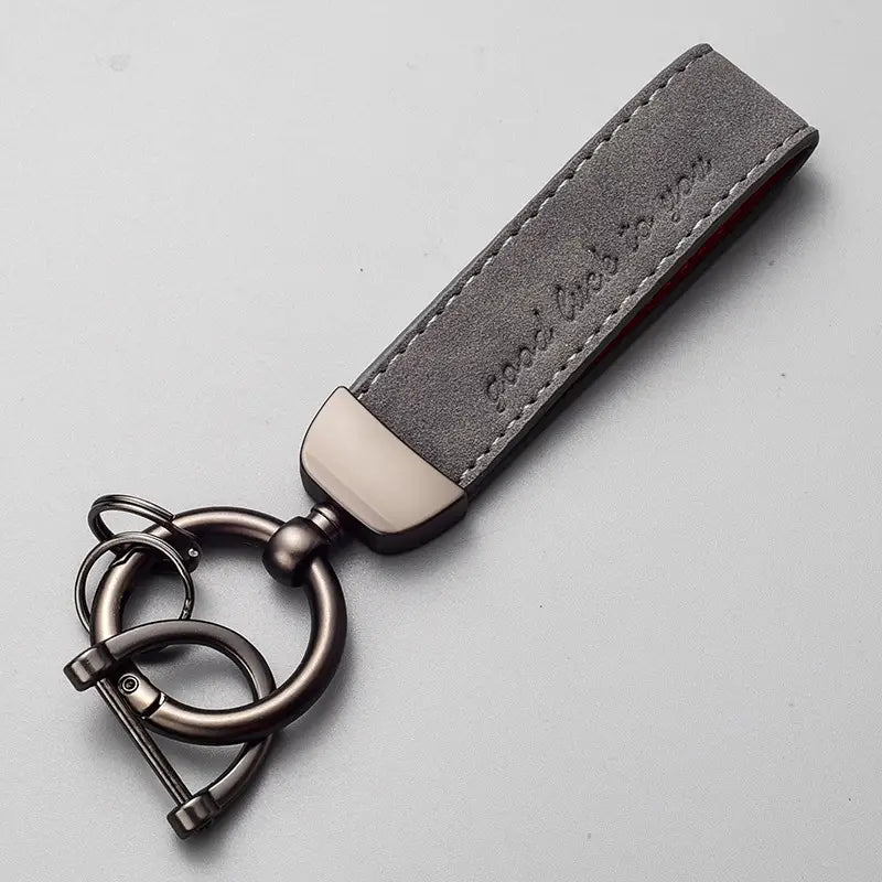 Gray suede leather car keychain with brushed metal ring and clasp featuring embossed text along the strap in genuine leather key ring design.