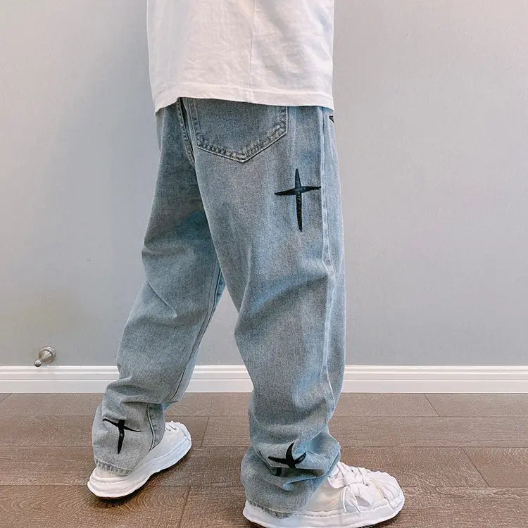 Face arrière d’un pantalon cargo en jean à jambes larges à effet délavé clair avec broderie croisée noire, sur la poche arrière et les poignets.