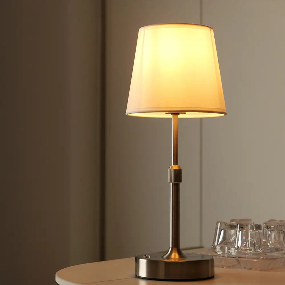 Plissierte Messing-Touch-Tischlampe mit einer warmtonigen Metallbasis, schlanker Stange und einem weichen cremefarbenen Stoffschirm, aus dem vorderen Winkel dargestellt