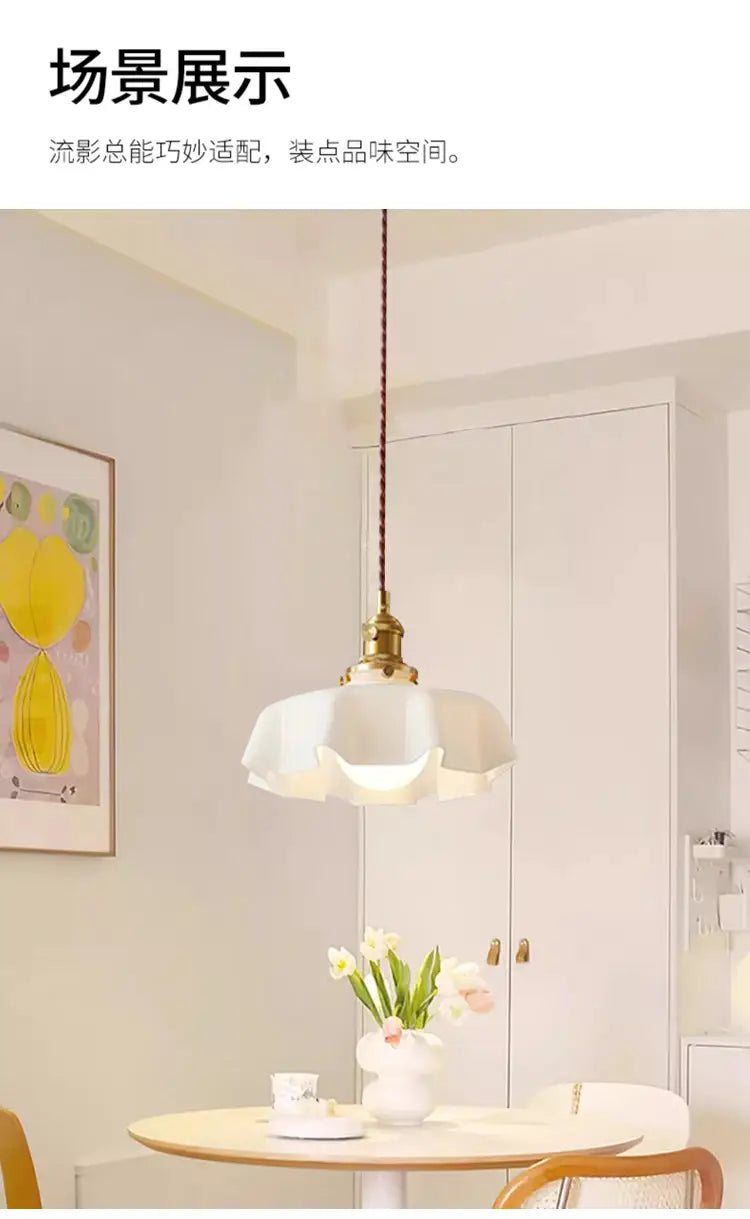Un luminaire suspendu délicat à jupe florale en verre blanc avec une tête de lampe en cuivre et un cordon tressé suspendu au-dessus d’une table à manger.