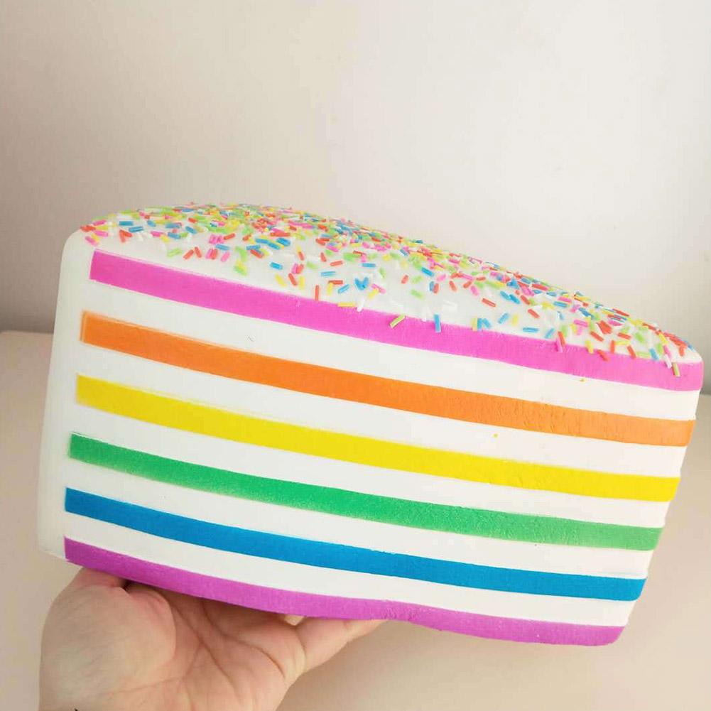 Un jouet antistress à gâteau arc-en-ciel à rebond lent, en forme d’un gâteau coloré rayé arc-en-ciel, avec un glaçage blanc et des vermicelles multicolores.