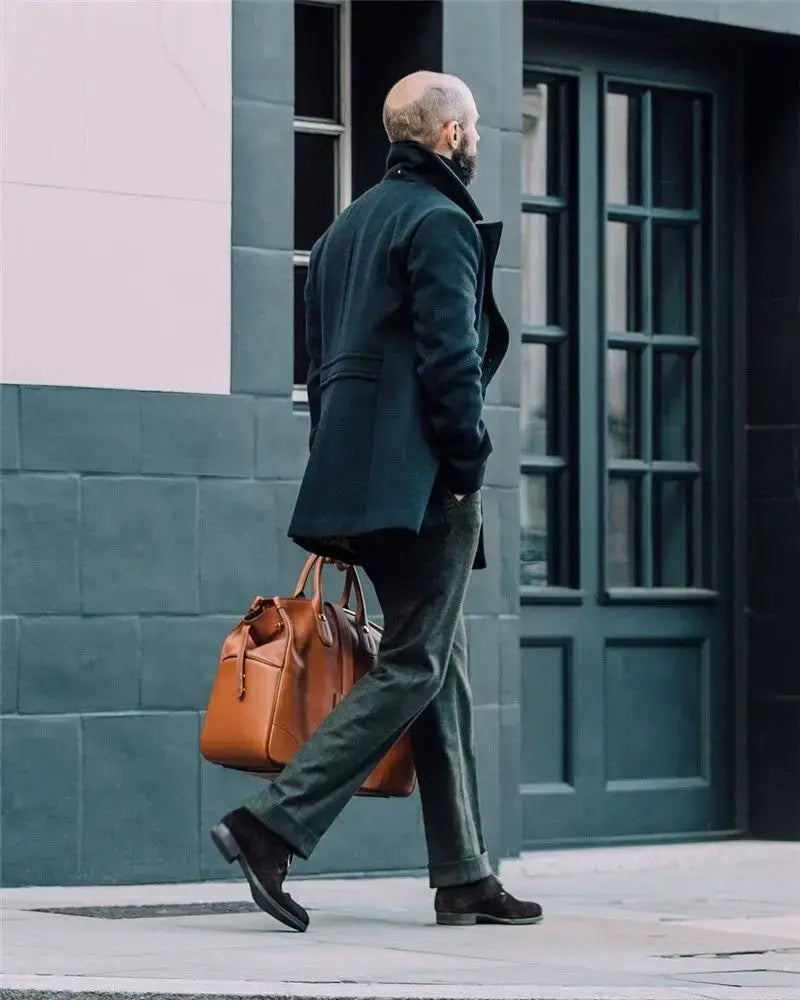 Portafolios de cuero marrón con asas superiores y un diseño estructurado que complementa el abrigo largo tipo peacoat de lana para hombre con doble botonadura y chaqueta de invierno.