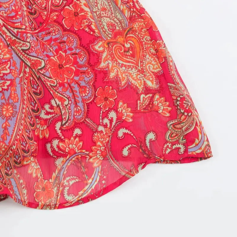 A vibrant red paisley halter top and midi skirt set made of sheer fabric with an intricate paisley and floral pattern in shades of orange, blue, and beige.